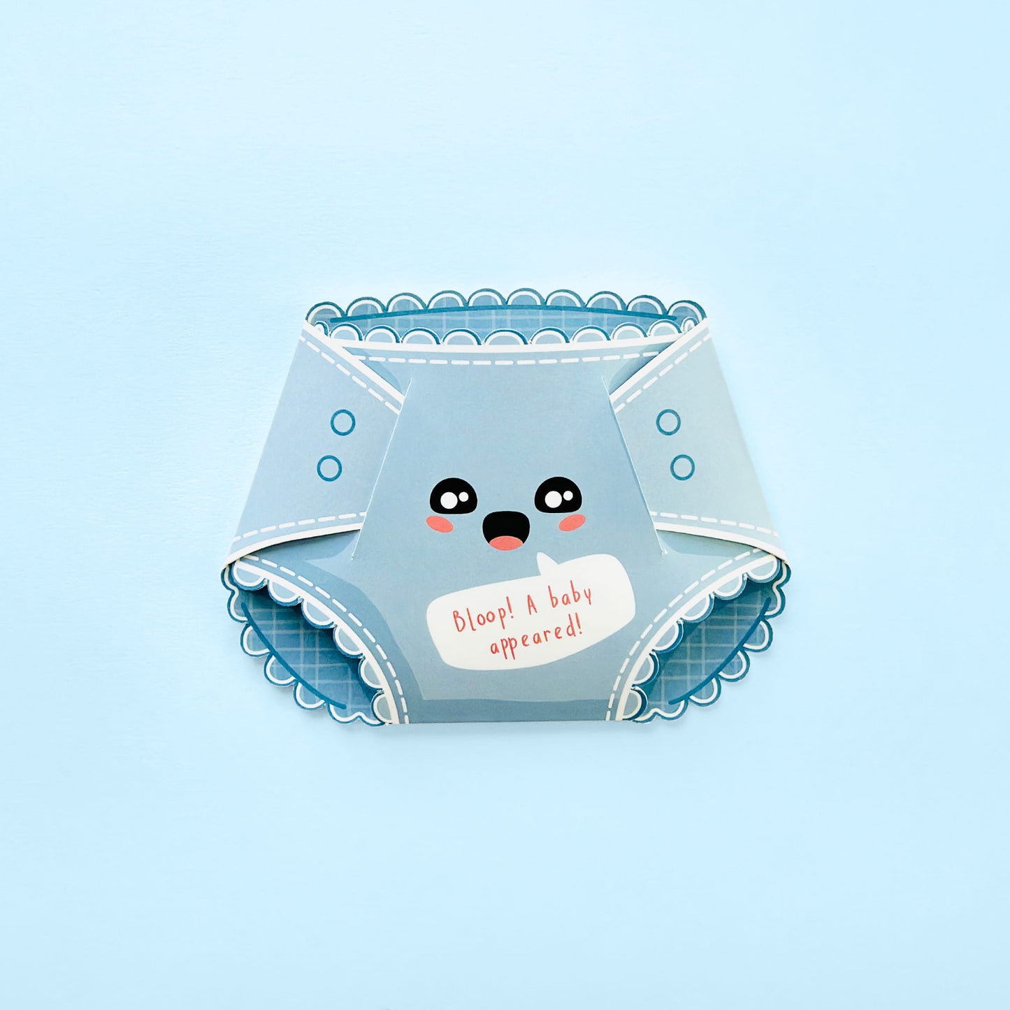 A light blue novelty diaper-shaped card with a cute cartoon face and the text 'Bloop! A baby appeared!' on a light blue background.