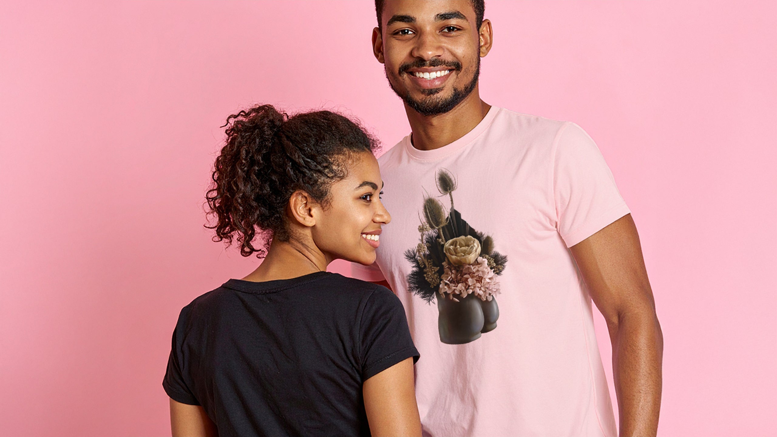 Two people standing side by side against a pink background, one wearing a black t-shirt and the other wearing a pink t-shirt with a cat graphic.