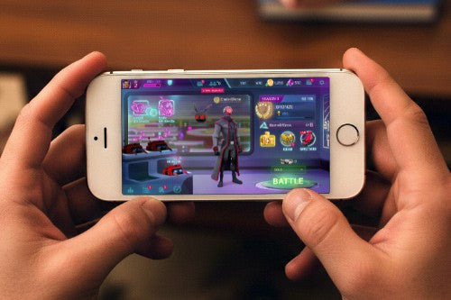 Person holding a smartphone playing a game with a character selection screen displayed.